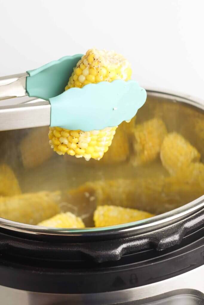 cooked corn held up by kitchen tong Instant Pot Sweet Corn Hot.